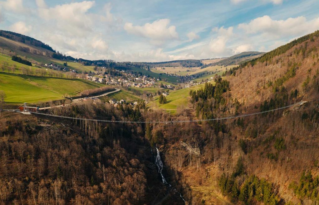 Die Hängebrücke spannt sich über das Tal, unter ihr der Wasserfall, dahinter die Häuser von Todtnau zwischen Wiesen