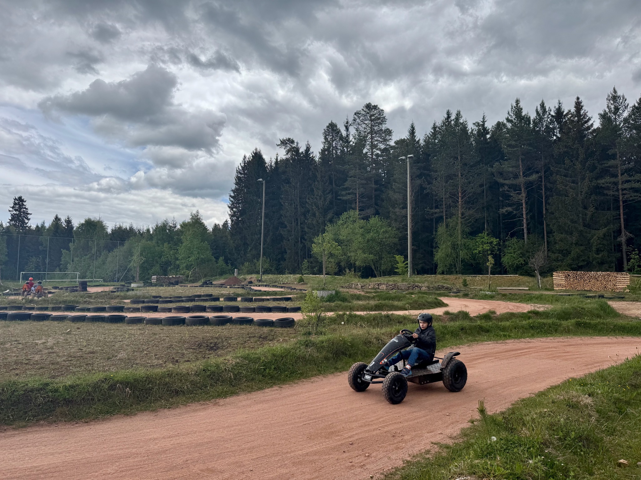 Der Offroad-Parcours am Gaspedal: ein Kind fährt mit dem Monster-Kart über die rote Sandpiste, links die mit Reifen abgesteckte Strecke, dahinter Wald und Holzstapel