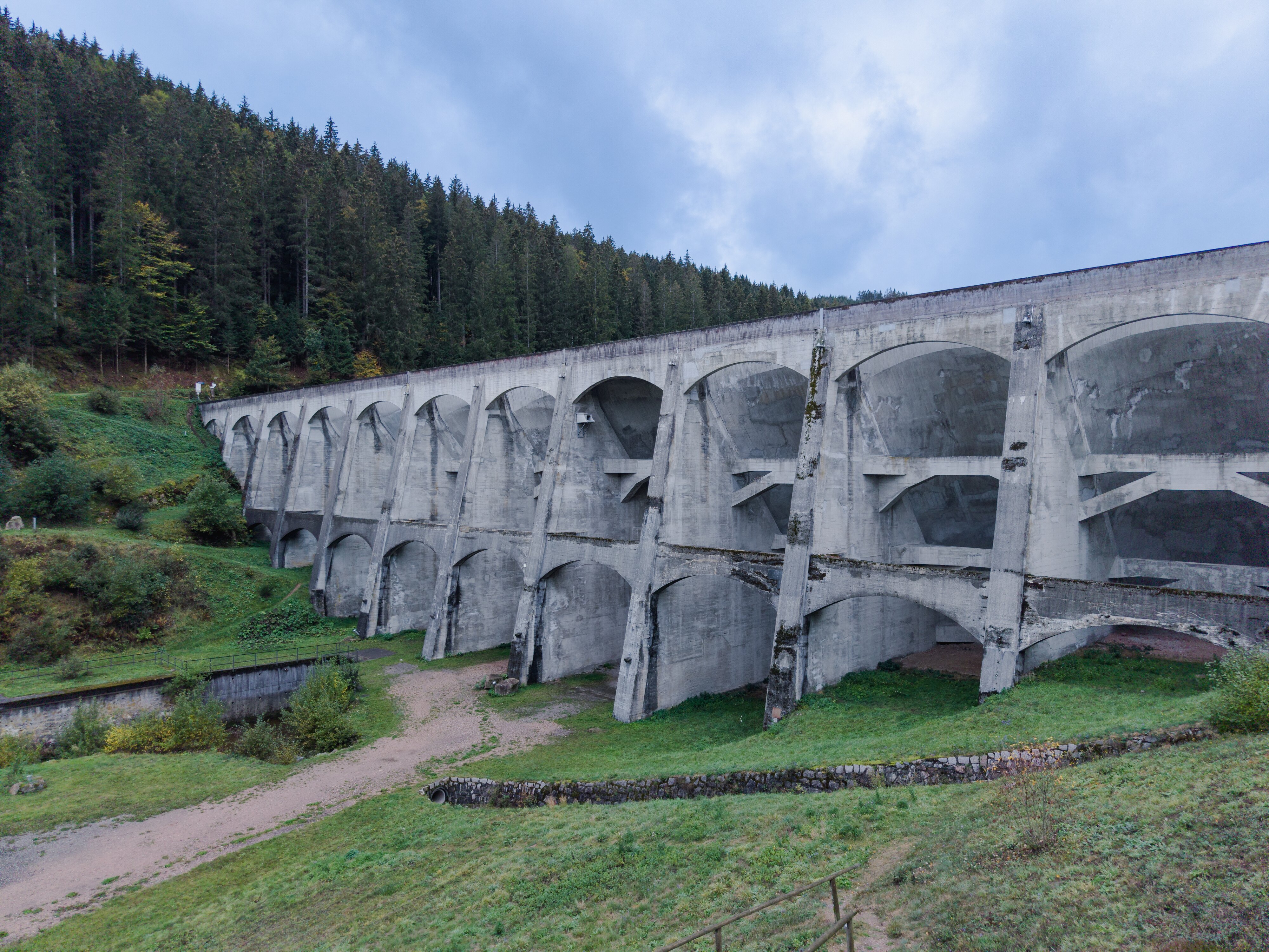 Die Gewölbereihenstaumauer der Linachtalsperre bei Vöhrenbach von der Luftseite: Bögen, Pfeiler und Streben vor einem Fichtenhang.