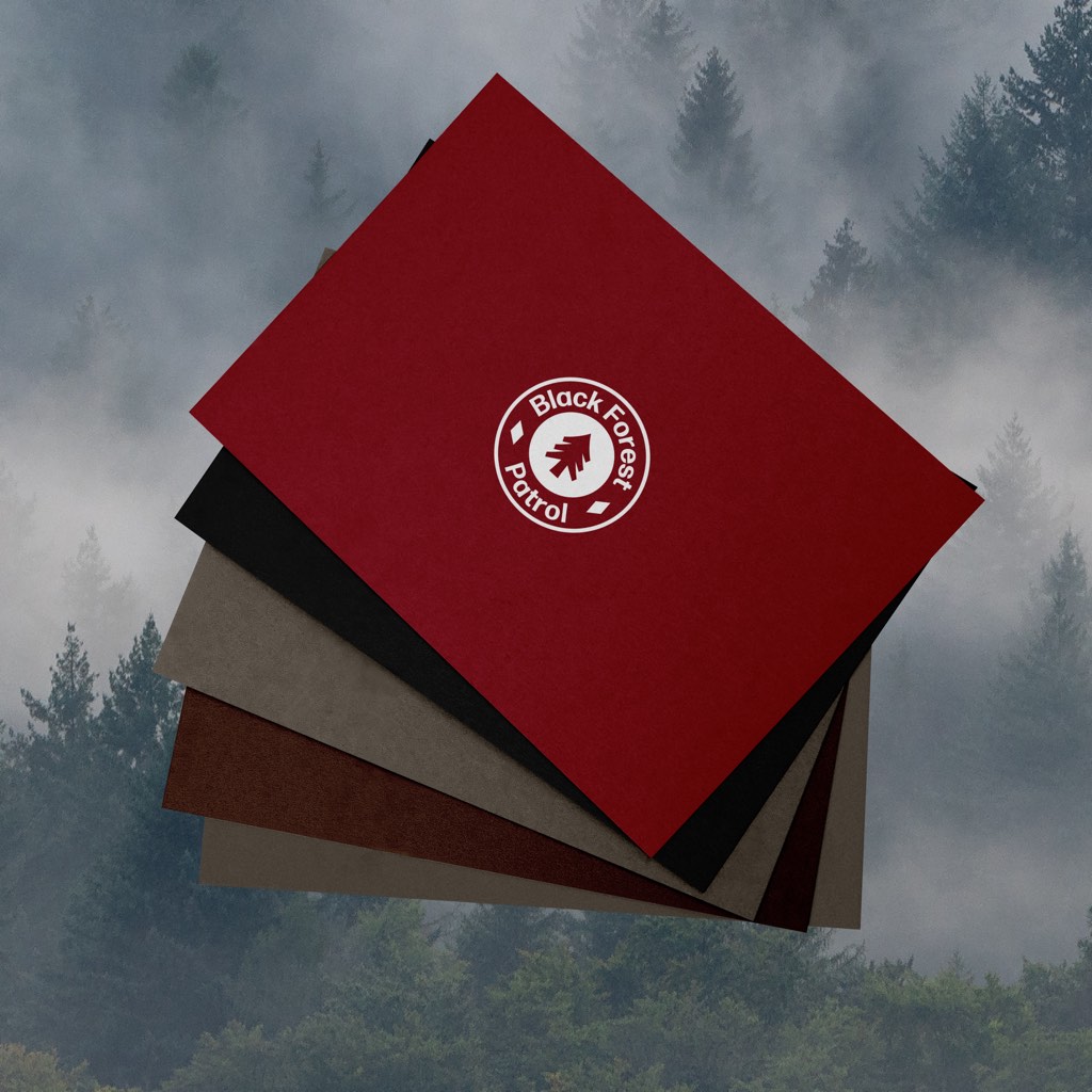 Fünf aufgefächerte Postkarten in Rot, Schwarz, Graubraun, Dunkelbraun und Beige, die oberste mit rundem weißem Zeichen, vor nebligem Tannenwald