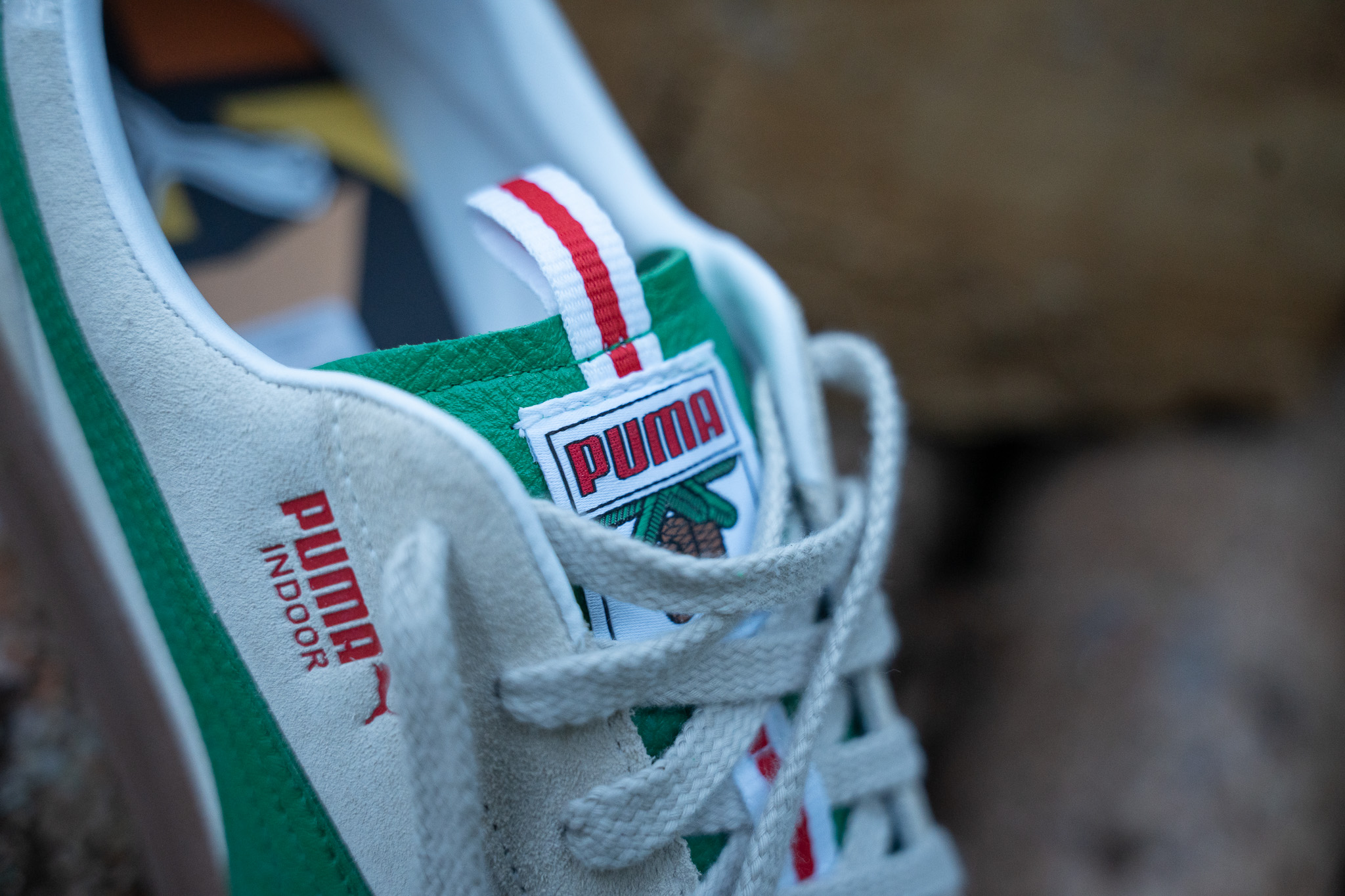 Nahaufnahme der Zunge des PUMA x Rothaus Indoor: Etikett mit PUMA-Schriftzug und Tannenzapfen, rot-weiße Lasche, seitlich der Schriftzug PUMA Indoor