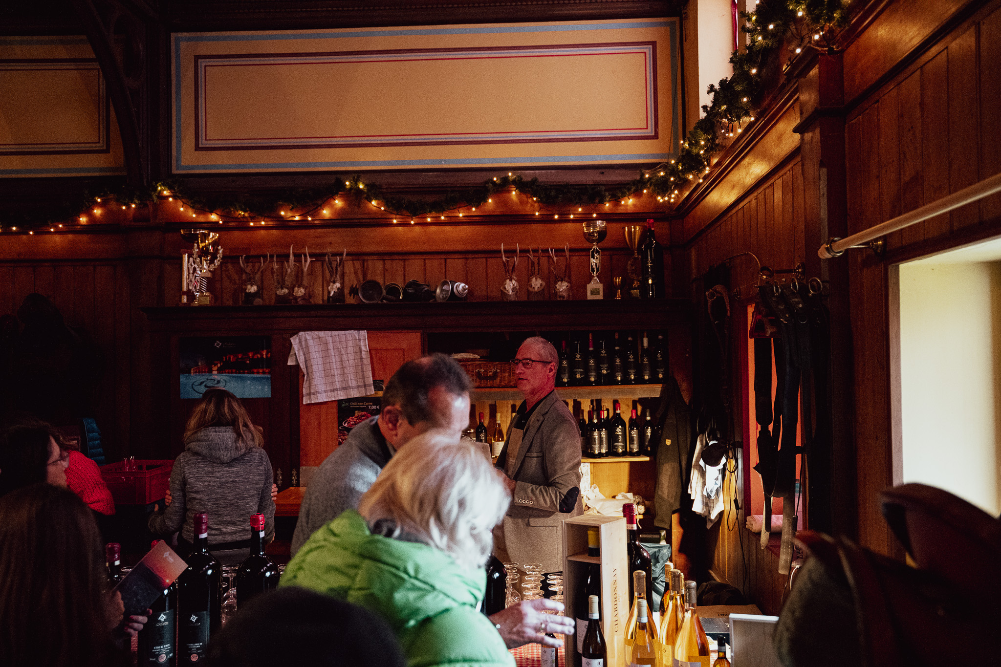 Holzvertäfelte Bar im Marstall: Weinflaschen im Regal, Pokale und Geweihe über der Theke, Lichterketten am Deckenrand, davor Gäste