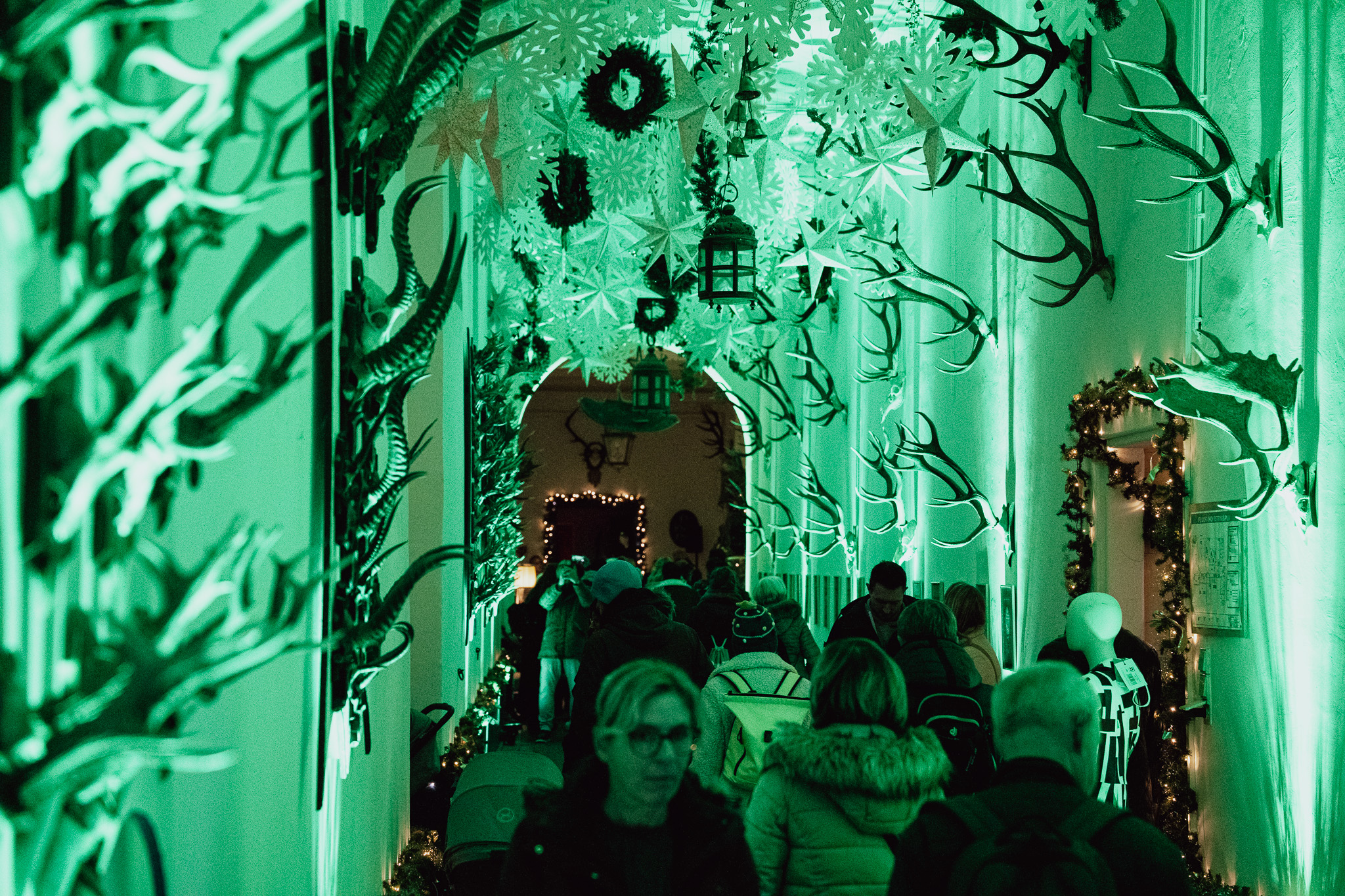Grün beleuchteter Gang der Fürstenberg Weihnachtswelt: an den Wänden Geweihe, unter der Decke Papiersterne und Laternen, dazwischen dicht gedrängte Besucher