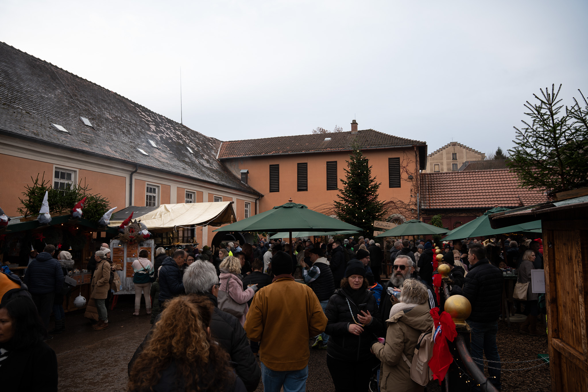 Innenhof des Fürstlich Fürstenbergischen Marstalls: Marktbuden mit Wichteln auf den Dächern, grüne Sonnenschirme, ein geschmückter Tannenbaum vor den Stallgebäuden